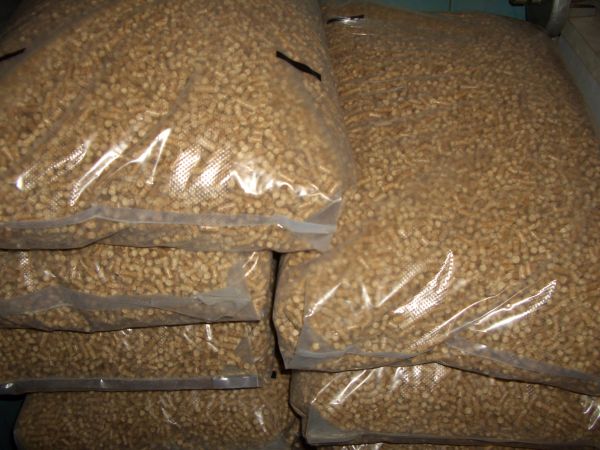 Stos worków wypełnionych jasnymi, cylindrycznymi granulkami, prawdopodobnie paliwem opałowym, widocznych przez przezroczyste opakowanie.